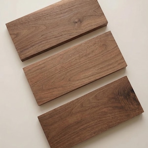 Puede incluir: Tres tablas de madera rectangulares, de color marrón oscuro y con vetas visibles. Las tablas están dispuestas de forma ligeramente escalonada, mostrando su textura y acabado natural. Las tablas miden aproximadamente 30 cm de largo.