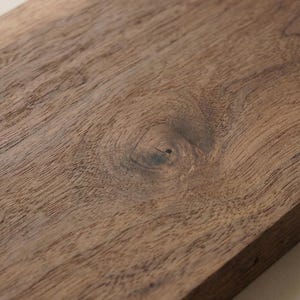 May include: Close-up of a rectangular wooden chopping board in a deep brown hue. The wood grain is clearly visible, with a knot feature in the centre. The board has a smooth, polished surface, indicating it's suitable for food preparation.