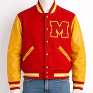 May include: A red and yellow varsity jacket with a large gold "M" on the chest. The jacket has yellow leather sleeves, gold buttons, and striped cuffs and collar. The jacket is displayed on a mannequin.