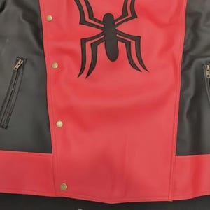 May include: Red and black jacket with a large black spider emblem on the chest. The jacket features a zipper pocket on each side and gold-colored snap closures. The jacket's design is a bold combination of red and black.