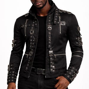 May include: Black jacket with multiple silver buckles and zippers. The jacket has a collared neckline and long sleeves. The model is wearing a black shirt and black jeans. The jacket is a unique fashion statement.