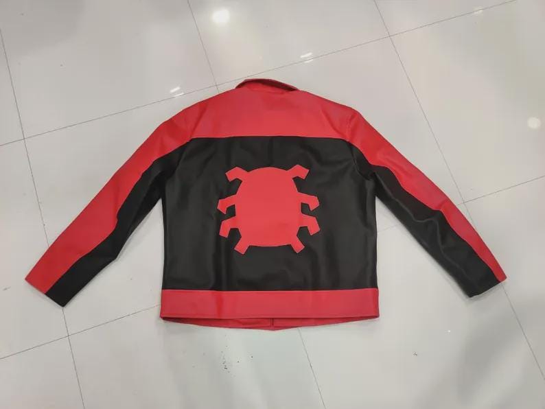 May include: Red and black jacket with a unique design. The jacket features a red upper section and sleeves, with a black central panel. A red emblem is centered on the back. The jacket has a classic collar and long sleeves.