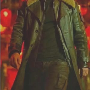 May include: A man wearing a long, olive-green leather coat with a shearling collar and a black shirt. The coat has a double-breasted design and a belt. The background is blurred with red lanterns.