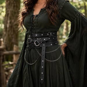 May include: A dark green long-sleeved dress with a lace-up front and flared sleeves, worn with a black multi-layered leather belt featuring silver-toned metal studs, buckles, and decorative hanging chains draped across the waist area.