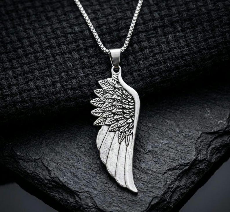 Silver angel wing pendant necklace with stainless steel chain displayed on a hand against a dark background, symbolic guardian angel jewelry and meaningful memorial gift.