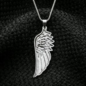 May include: A silver-toned metal pendant shaped like a single bird wing, featuring detailed feather textures and a smooth border. The pendant hangs from a matching silver-toned box chain necklace, showcasing a metallic finish and a structured design.