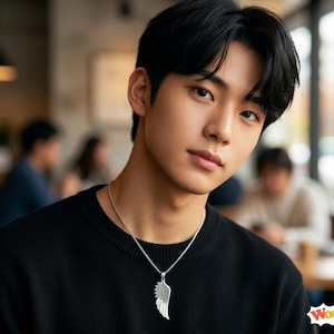 May include: A silver-toned necklace featuring a detailed wing-shaped pendant with textured feather patterns, suspended from a thin metallic chain, worn against a plain black sweater. The pendant has a distinct curved shape and metallic finish.