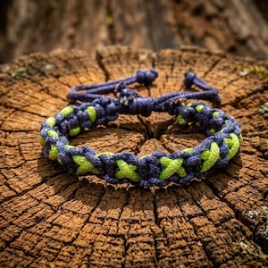 Puede incluir: Pulsera hecha a mano con diseño trenzado en azul marino y verde neón. La pulsera tiene un cierre ajustable en azul marino. Se muestra sobre una superficie de madera envejecida. El diseño son nudos entrelazados.