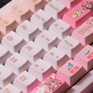 May include: Close-up of a custom mechanical keyboard with pink and white keycaps. The keycaps feature various symbols and text, including "ALT" and "SHIFT". Some keycaps have anime-style illustrations. The keyboard has a pastel color scheme.