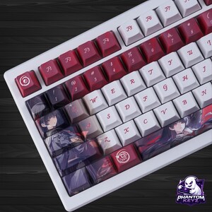 May include: White mechanical keyboard with red and white keycaps. Some keycaps feature anime-style illustrations. The keyboard has a white frame and a variety of function keys. The keyboard is angled, showing the keys in detail.