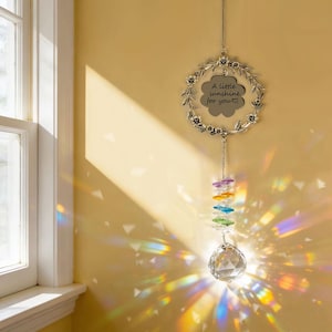 May include: A decorative suncatcher with a silver floral wreath and a cloud-shaped charm that reads "A little sunshine for you." Below the charm hangs a strand of colorful crystals and a clear crystal ball.