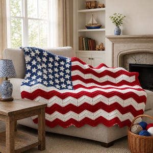 May include: A crocheted blanket draped over a sofa, featuring a design resembling the American flag. The blanket showcases a blue field with white stars and red and white chevron stripes. The sofa is beige, and the room has a cozy, inviting atmosphere.