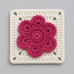 May include: A square, off-white crocheted granny square with a magenta flower in the center. The flower has a circular center with six petals. The square has four corner holes. This handmade item is suitable for various craft projects.