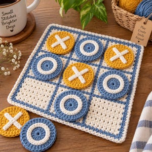 May include: A square, off-white crocheted tic-tac-toe board with blue grid lines. The game includes circular pieces in mustard yellow with white stitched X designs and blue with white stitched O designs, arranged on the board.