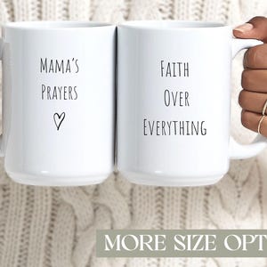 Puede incluir: Dos tazas de cerámica blanca con texto negro. Una taza dice "Mama's Prayers" con un símbolo de corazón, la otra dice "Faith Over Everything". Las tazas tienen asas grandes y están sostenidas por manos con anillos. El fondo tiene el texto "MORE SIZE OPTIONS."