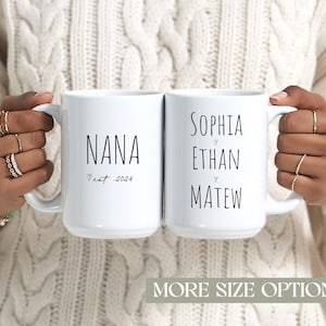 Puede incluir: Dos tazas de cerámica blancas con texto negro. Una taza dice "NANA" con "est. 2024" debajo. La otra taza dice "SOPHIA", "ETHAN" y "MATEW". Las tazas son sostenidas por una persona que lleva anillos.