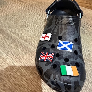 May include: A white ceramic mug with a black handle and the text "But First, Coffee" in a bold, black font. The mug is set against a blurred background, suggesting a cozy setting.