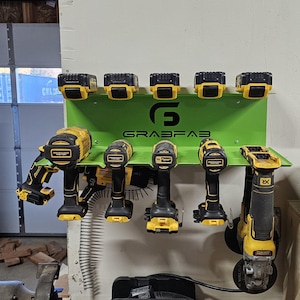 Op de afbeelding: Een limoengroene metalen wandhouder voor elektrisch gereedschap met het zwarte GrabFab-logo. Het rek houdt vijf geel-zwarte accu's voor draadloos gereedschap op de bovenste plank en vijf geel-zwarte elektrische gereedschappen hangen eronder.