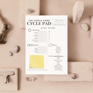 May include: A white cycle pad with the text "THE SIMPLE HOME CYCLE PAD" and a yellow sticky note. The pad includes sections for tracking daily habits and a "To Do or Don't" list. The background includes decorative elements.