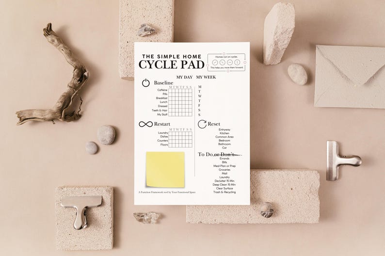 May include: A white cycle pad with the text "THE SIMPLE HOME CYCLE PAD" and a yellow sticky note. The pad includes sections for tracking daily habits and a "To Do or Don't" list. The background includes decorative elements.