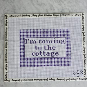 May include: A white needlepoint canvas with a purple gingham border and the text "I'm coming to the cottage." The words are in a purple font. The canvas is surrounded by the text "Sleepy Girls Stitching."
