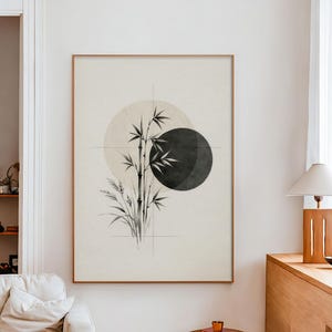 May include: A framed art print featuring a minimalist design with bamboo stalks, grass, and two overlapping circles in shades of gray and beige. The artwork is set against a light background and framed in a thin, light brown frame.