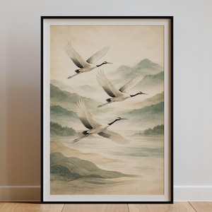 May include: Framed art print featuring three cranes in flight over a misty landscape. The birds have white feathers with black accents and red markings. The background depicts mountains and water in muted green and beige tones.