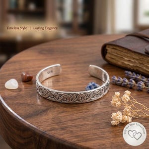 May include: A silver cuff bracelet featuring an embossed swirling pattern and the hallmark 925 stamped on the inner band. The bracelet is open-ended and displays a metallic finish with dark oxidised detailing within the engraved spiral motifs.