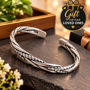 Può includere: Un bracciale a fascia in argento con un design a corda intrecciata e finitura ossidata. L'interno del bracciale è chiaramente stampato con il testo S925. Un grafico circolare nell'angolo in alto a destra mostra il testo Gift FOR YOUR LOVED ONES.