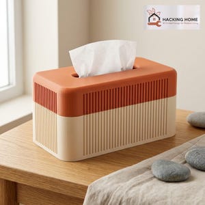 May include: A rectangular tissue box cover featuring a two-tone design with a burnt orange top section and a cream-colored base. The exterior has vertical ribbed detailing on all sides. A white tissue is pulled through the top opening.