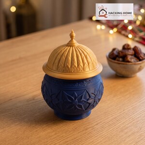 May include: A dark blue lidded jar with a matte finish and embossed floral patterns, topped with a gold-colored dome lid featuring a pointed finial. The text HACKING HOME 3D Printed Design for Modern Living is visible in the corner.