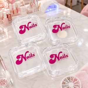 Puede incluir: Cuatro cajas de almacenamiento cuadradas de pl&aacute;stico transparente con tapas abatibles. Cada caja presenta el texto rosa intenso "Nails by Sophia" impreso en la parte superior, con "est. 2026" en una fuente m&aacute;s peque&ntilde;a. Los recipientes son transparentes.