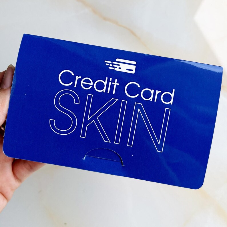 May include: A blue rectangular product with the words "Credit Card SKIN" in white. The product has a credit card icon in the upper right corner. The product is held by a person.