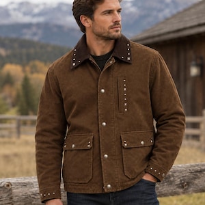 May include: A brown jacket featuring a dark brown corduroy collar, silver-toned metal snap buttons, and small silver square studs along the collar, chest pocket, cuffs, and flap pockets. The jacket is worn over a dark sweater and blue jeans.