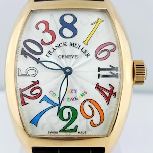 Peut inclure: Une montre Franck Muller Crazy Dreams dorée avec un cadran blanc et un bracelet en cuir marron. La montre présente des chiffres colorés surdimensionnés et les mots "Franck Muller Geneve", "Crazy Dreams", "Swiss Made".