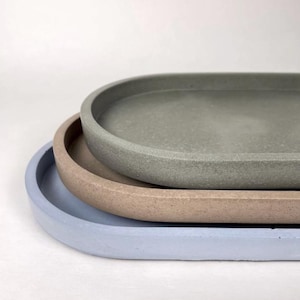 May include: Three oval trays stacked, each in a different colour. The top tray is a muted green, the middle tray is tan, and the bottom tray is light blue. The trays have a smooth, matte finish.