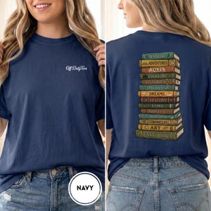 May include: A navy blue t-shirt featuring the white text Off Duty Tees on the front left chest. The back displays a vertical stack of colorful illustrated books with titles including Nature, Adventures, Tales, Folklore, Stories, Myths, Dreams, History, Lore, Novels, Theory, Chronicles, Art, and Last Book.
