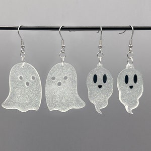 以下が含まれることがあります： 白いグリッターの幽霊チャームが付いた銀のイヤリングが4ペア。幽霊の2つは黒い目と笑顔の口、もう2つは黒い点で目を表現しています。