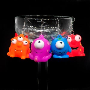 May include: Four pairs of colorful monster earrings. Each earring features a different monster design with a single or multiple eyes, and a variety of colors including orange, pink, blue, and red.