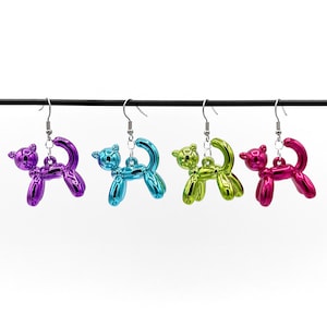 May include: Four pairs of balloon animal earrings. The earrings are silver and feature a metallic balloon animal shaped like a dog in purple, blue, green, and pink.