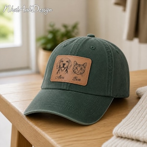 May include: A dark green baseball cap featuring a rectangular tan leather patch on the front. The patch displays a black line-art illustration of a dog and a cat, with the names Alex and Ben engraved below each respective animal portrait.