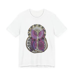 Könnte beinhalten: Weißes T-Shirt mit einem farbenfrohen, geometrischen Eulen-Design. Die Eule besteht aus konzentrischen Kreisen in Lila, Rosa und Gold, die ein Mandala-ähnliches Muster bilden. Das Design ist mittig auf der Vorderseite des Shirts platziert.