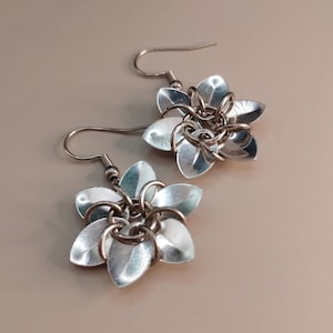 Könnte beinhalten: Ein Paar silberfarbene Blumenohrringe. Jeder Ohrring hat ein Blumendesign mit fünf Blütenblättern und einem kettenartigen Mittelteil. Die Ohrringe haben einen Hakenverschluss.