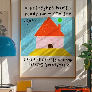 Op de afbeelding: Een ingelijste kunstafdruk met een kleurrijke, kinderlijke illustratie van een huis met de tekst "A refreshed home, ready for a new sea -Son." en "The little things at HOME: finding small joys."
