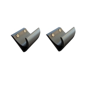 May include: Two black metal U-shaped brackets with rounded edges and two screws each. The brackets are designed to be mounted on a surface. The image is taken against a white background.