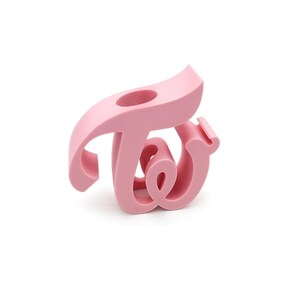 May include: A light pink, stylized sculpture of the word "TWICE". The sculpture is a single piece with a curved, flowing design. The object is made of a solid material and has a smooth, matte finish.