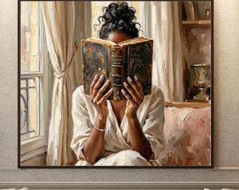 May include: A framed wall art print depicting a person with dark hair in a bun, wearing a light-coloured robe, holding an open dark-covered book in front of their face. The scene is set indoors near a window with curtains and a shelf with a vase.