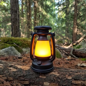 Puede incluir: Una linterna negra con un brillo amarillo cálido, sobre un fondo de bosque. La linterna tiene un diseño clásico con un asa y un botón en la base. Está apoyada sobre un tronco marrón.