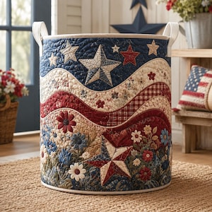 May include: A cylindrical fabric laundry basket featuring a quilted patriotic design with red, white, and blue colors. The exterior displays wavy patterns, floral motifs, and large star shapes. It includes two white fabric handles on the sides.