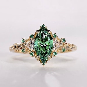 May include: A gold ring featuring a large, marquise-cut green gemstone as the centerpiece. The ring is adorned with smaller green and clear gemstones, set in a detailed, ornate design. The band has a textured, braided appearance.